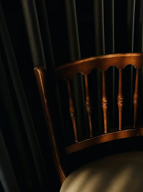 a wooden chair sitting in front of black curtains
