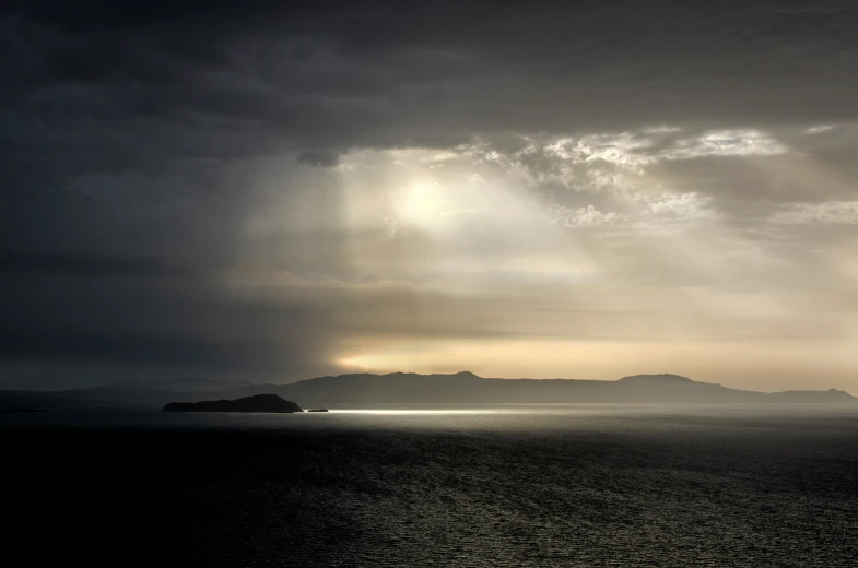 the sun is shining through some dark clouds over a body of water