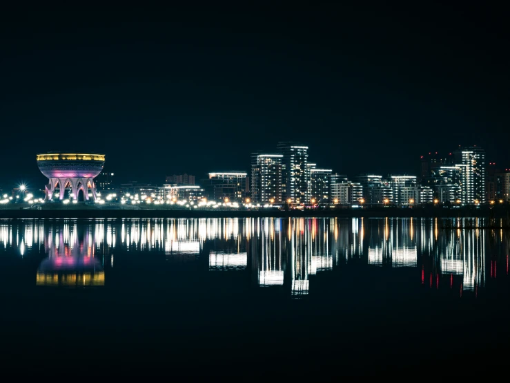 the lights are on and reflect off of the buildings in the water