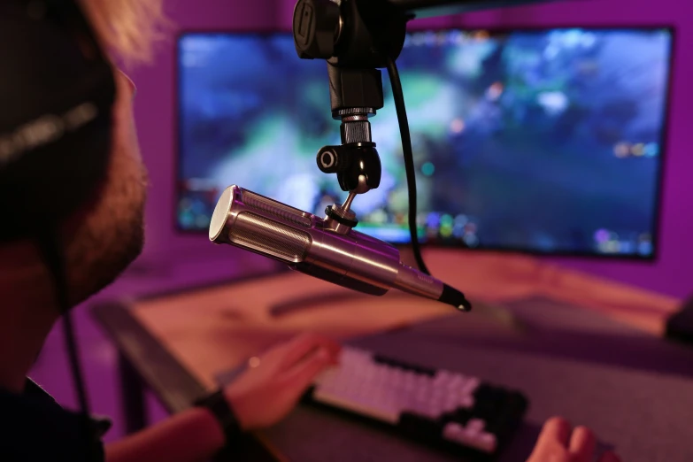 a recording microphone sits on a desk as someone uses a laptop computer behind it