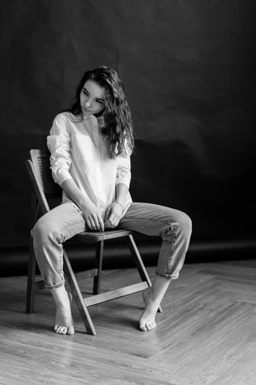 a girl sits on a wooden chair with her legs crossed