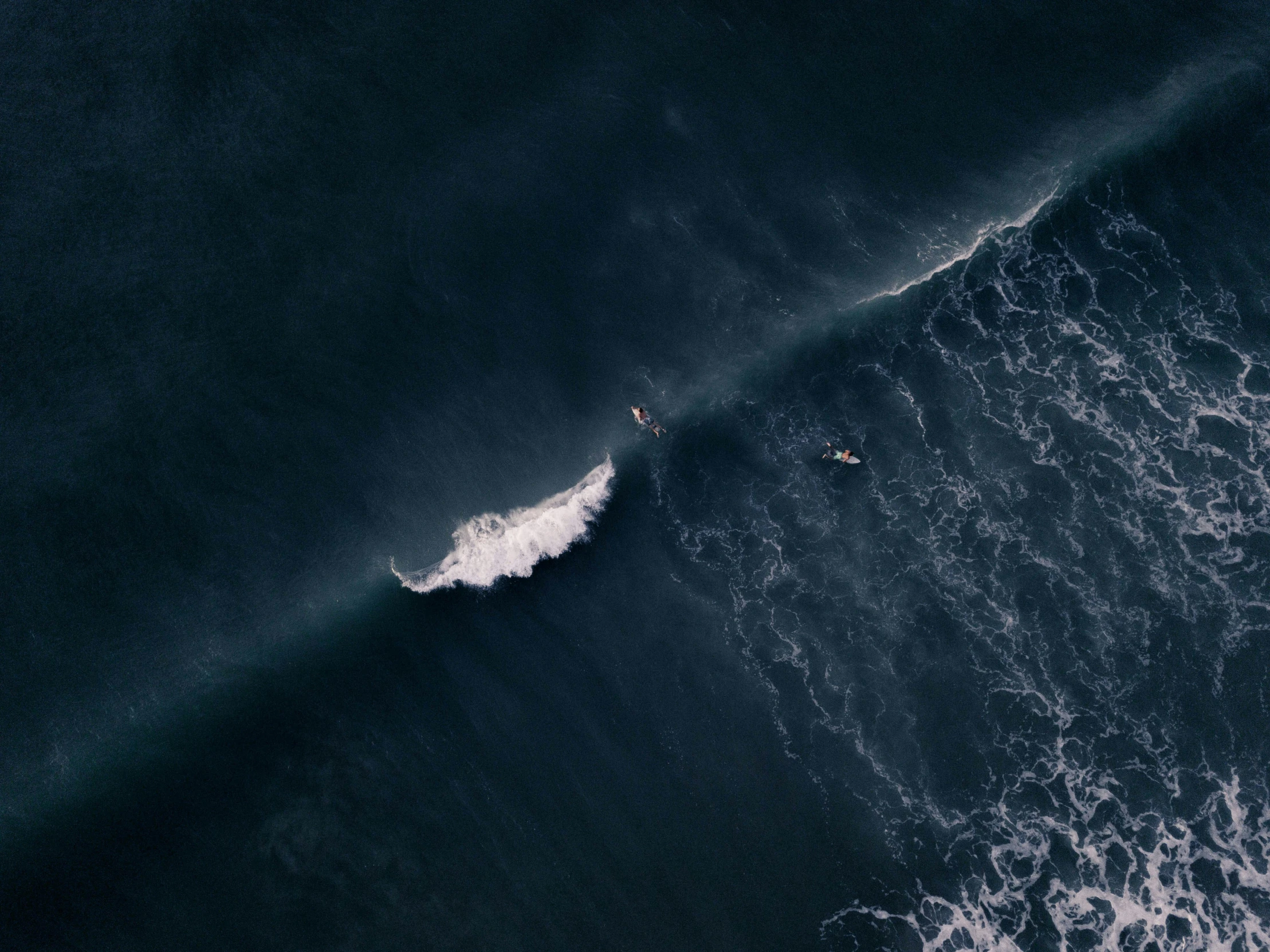 an aerial view of surfers riding waves off the coast