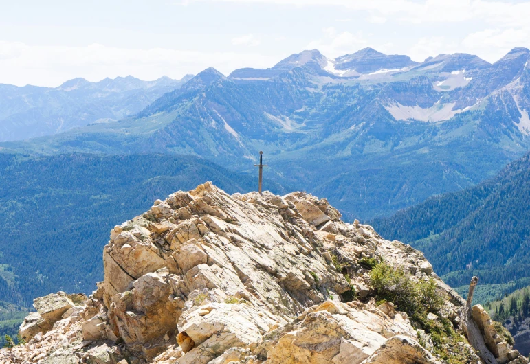 the cross is on the edge of the rock in front of the mountains