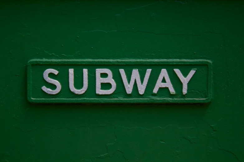 a subway sign is mounted on a green wall