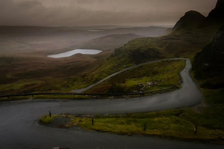 a curved road next to a mountain and lake