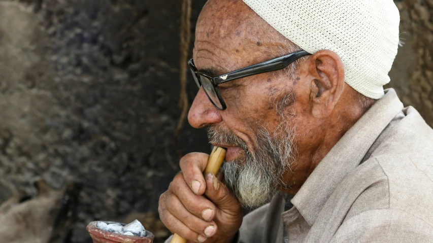 an older man wearing glasses and a white cap smoking a cigarette