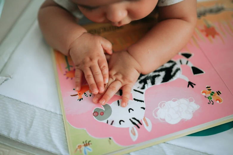 baby looking at her hand and kneading on a pink book