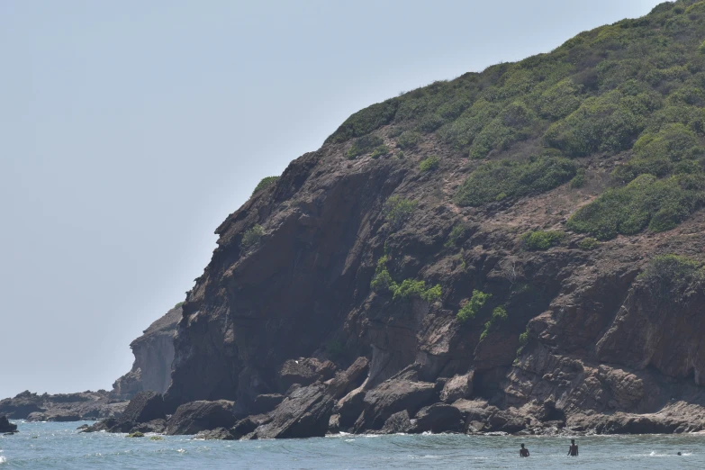 several people are surfing in the ocean near a large rock