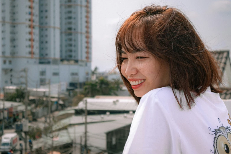 an attractive young woman with bangs smiles on a rooftop