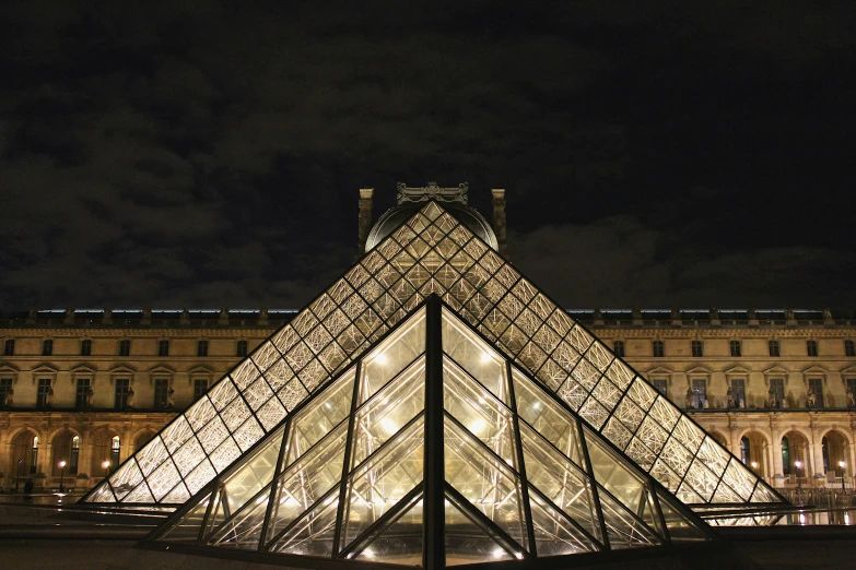 a pyramid structure in front of a large building at night