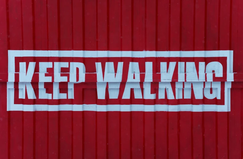 a sticker on the side of a red wall reads keep walking