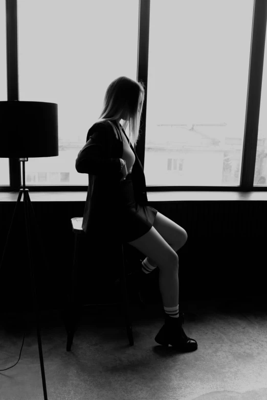 black and white pograph of woman sitting on chair looking out window