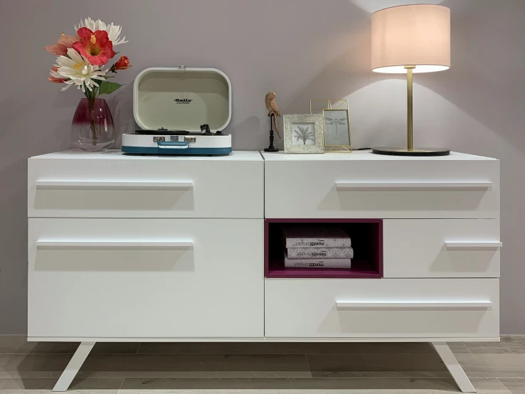 a white dresser with a lamp, vase and pos on top