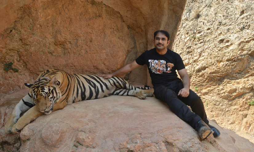 a man with black pants and a shirt poses next to a tiger on a rock