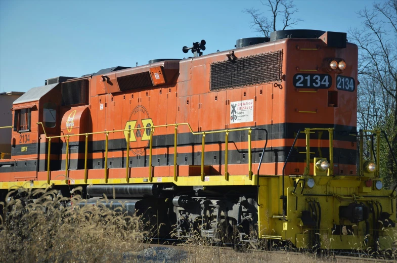 a train that is orange with black stripes sitting on the tracks