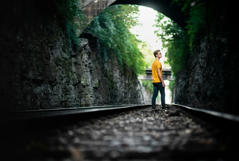 a boy in yellow shirt standing on railroad tracks