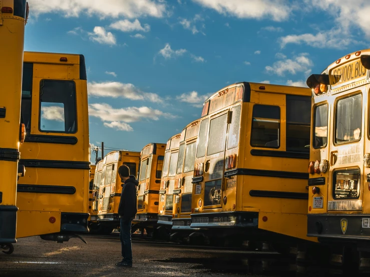 the person standing next to many yellow school buses