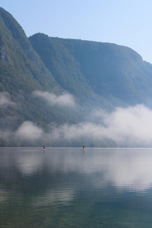 two men on the water standing on a boat in a misty lake