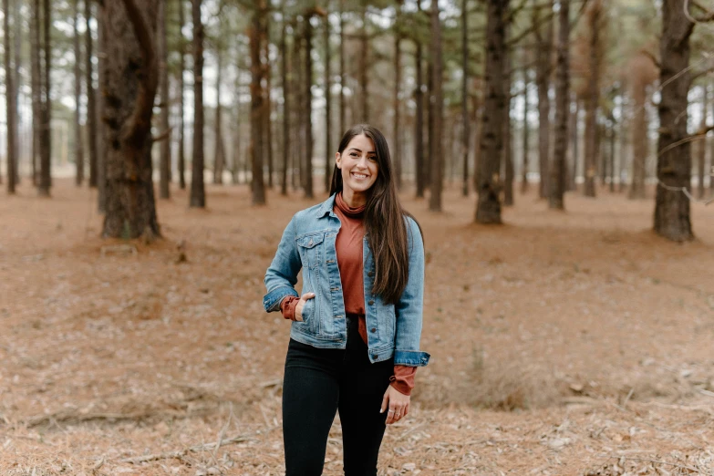 a woman in black jeans standing in front of a forest