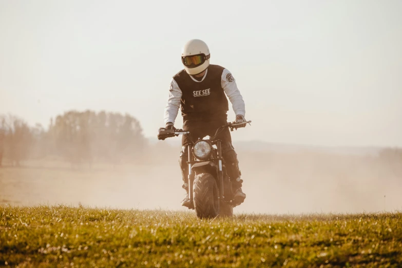 motorcyclist in white helmet, full uniform and black leather jacket standing near grassy area in field