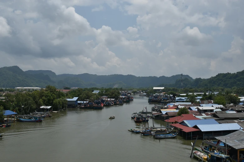 a river with small boats, some standing, houses and mountains in the background