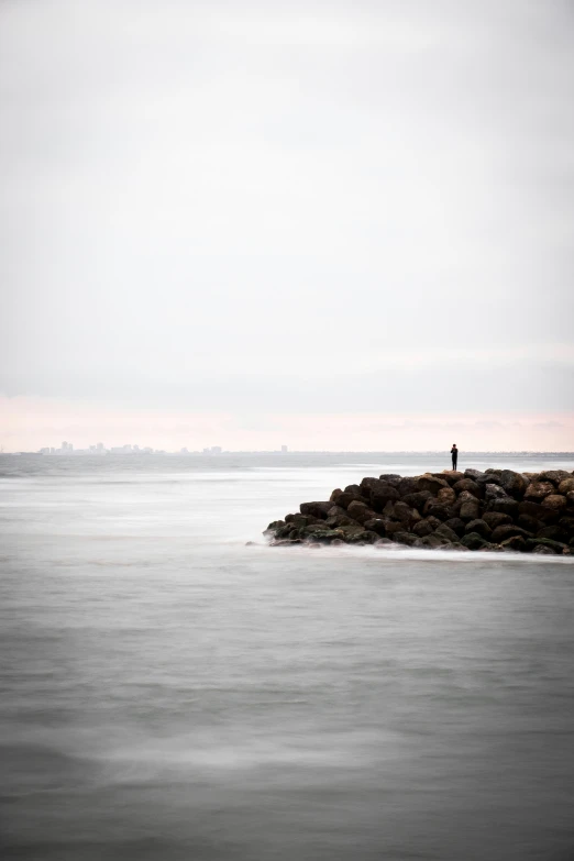 a lone man standing on a rock in the middle of the ocean