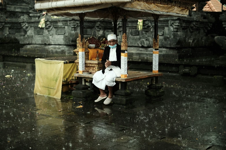 two people sitting under a wooden platform in the rain