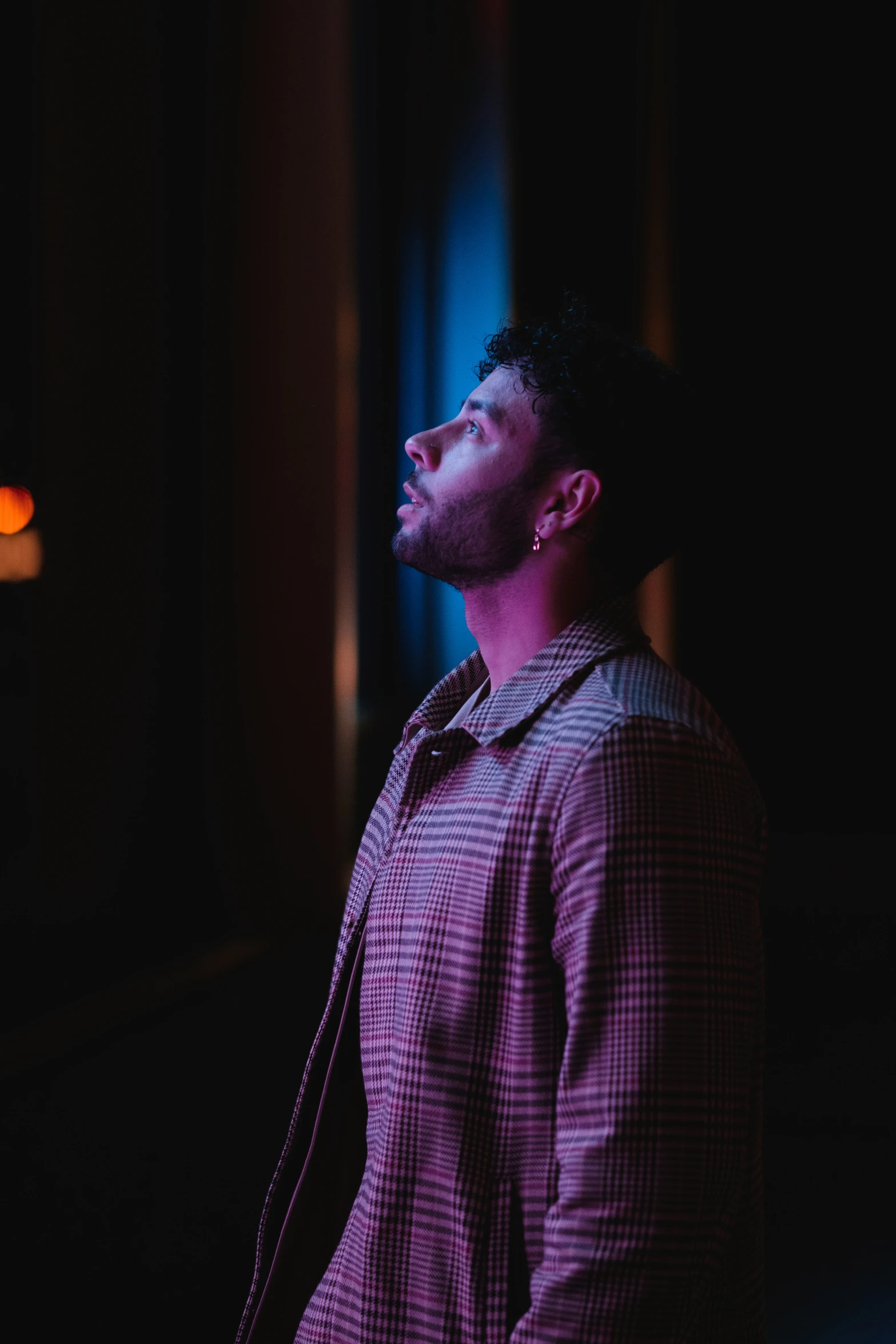 a young man stands in the dark with his eyes closed