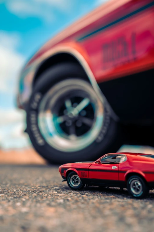 a red toy car on the ground in front of a red toy car