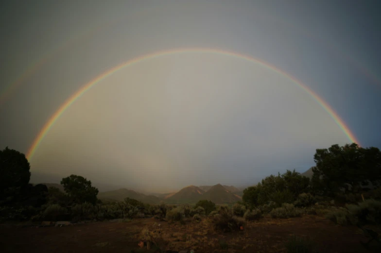 two rainbows shine in the sky over some trees