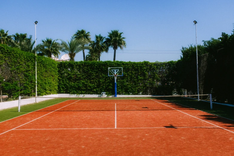 an empty tennis court sits in front of some trees