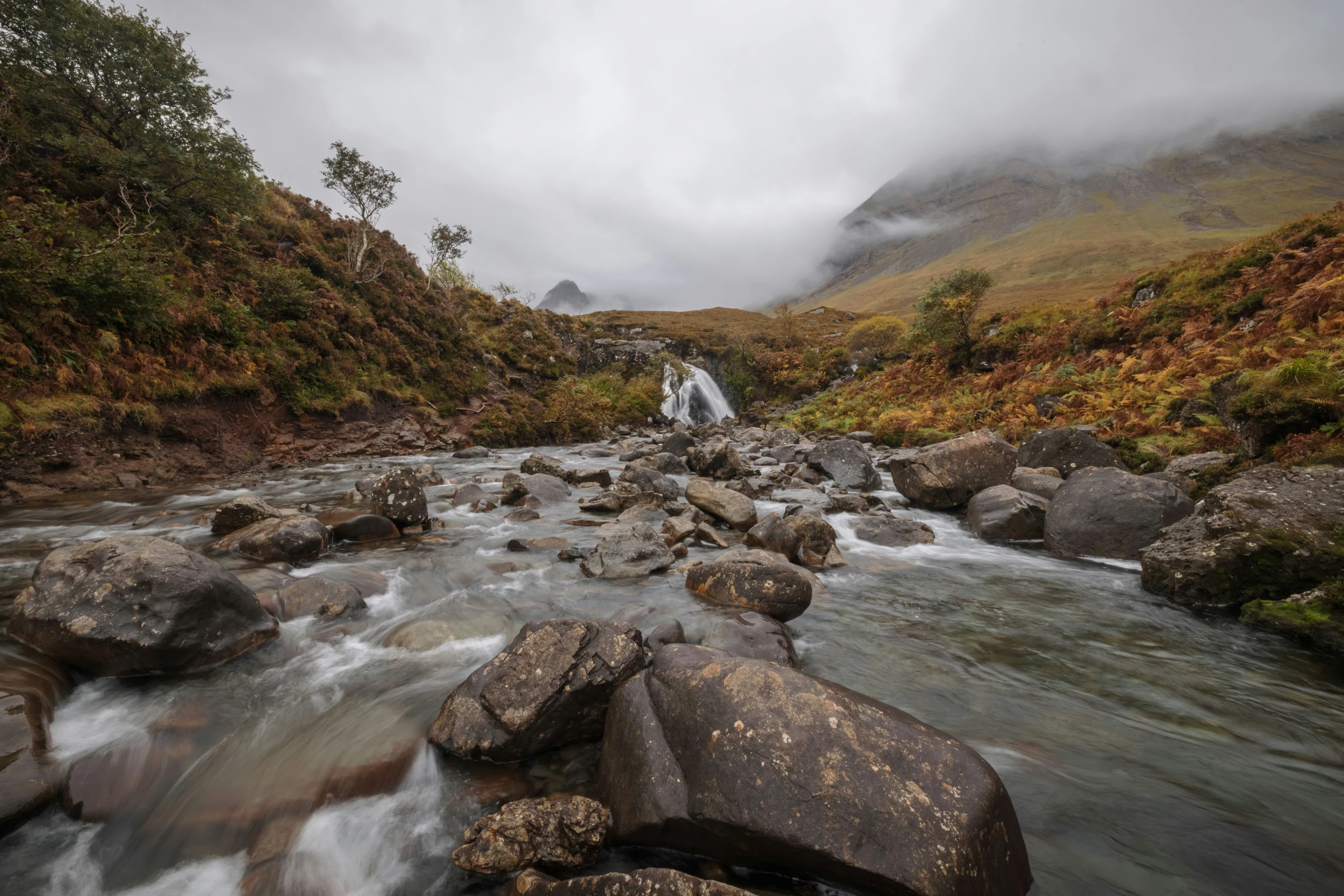 a river runs between the mountains and the grassy hills