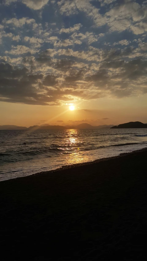 the sun rises over the ocean with small island in distance