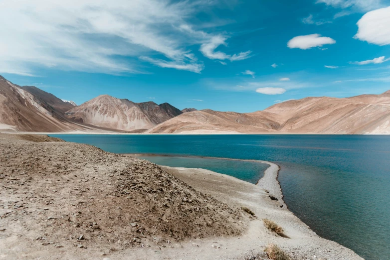 there is an ocean with sand and mountain side near the shore