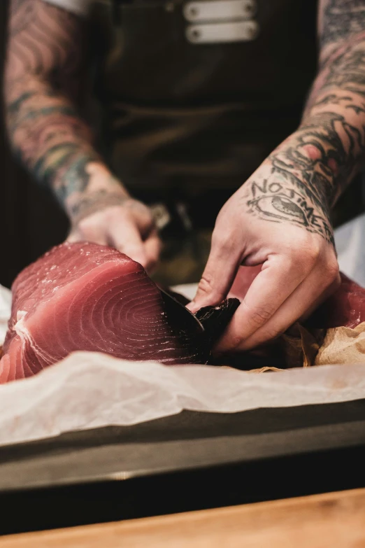 tattooed man slicing up fish on a wooden  board