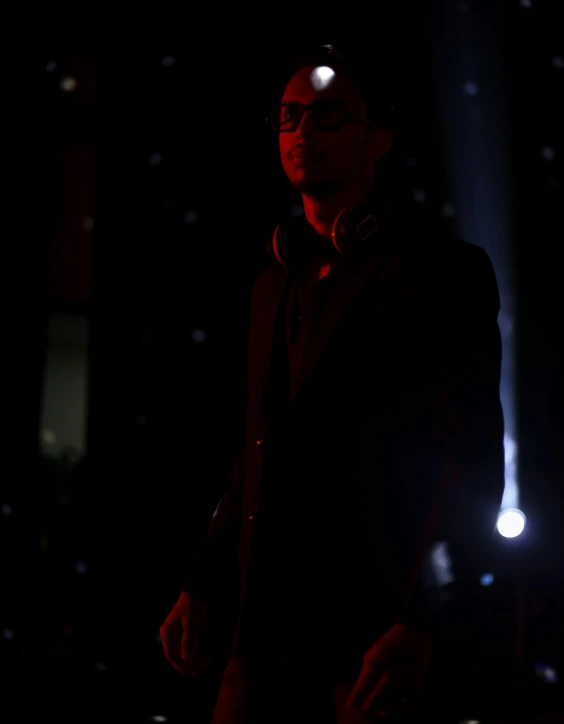 a young man wearing glasses and a black jacket looks toward the camera at night
