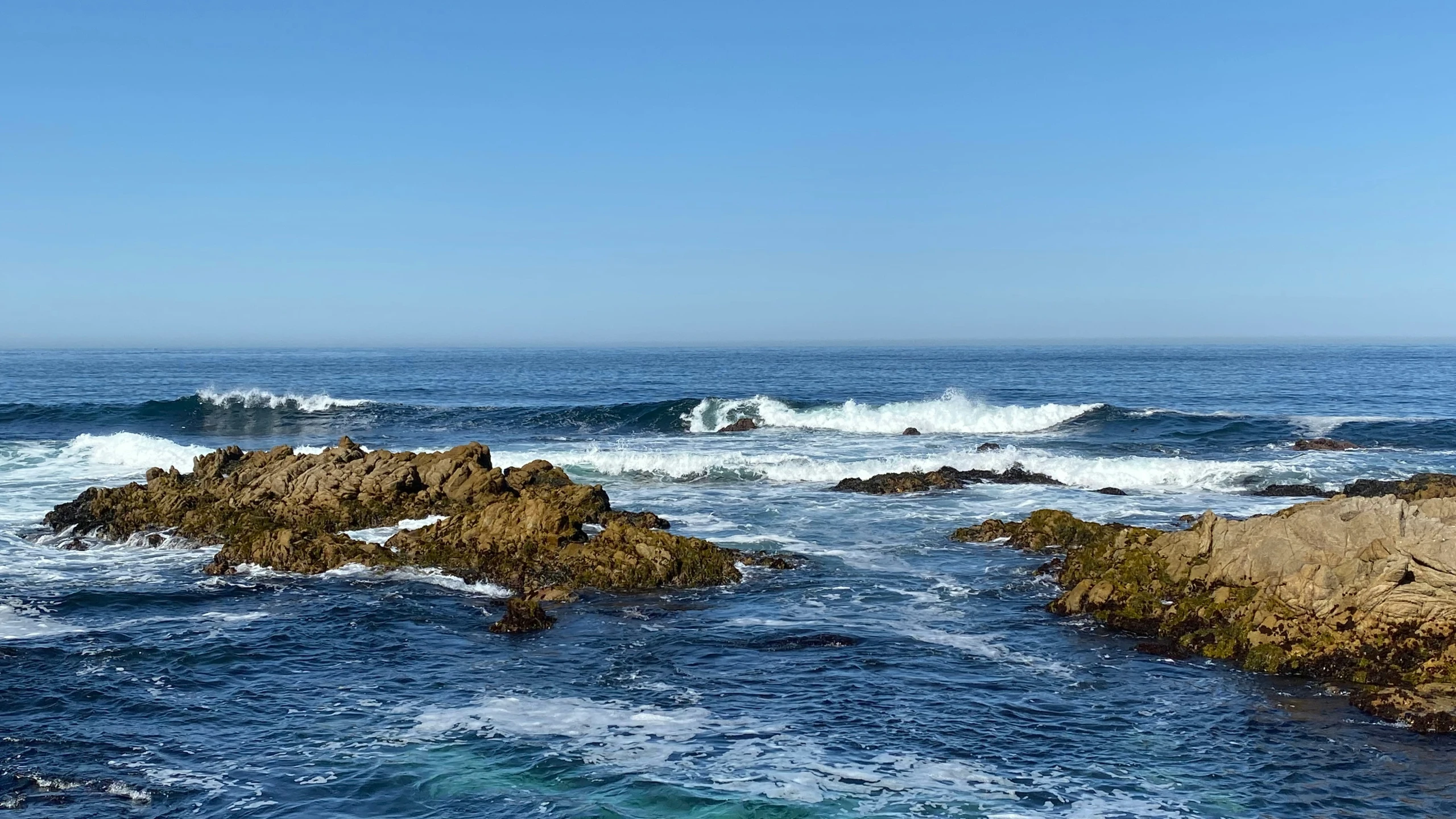 waves crashing against a rocky shore line on a sunny day