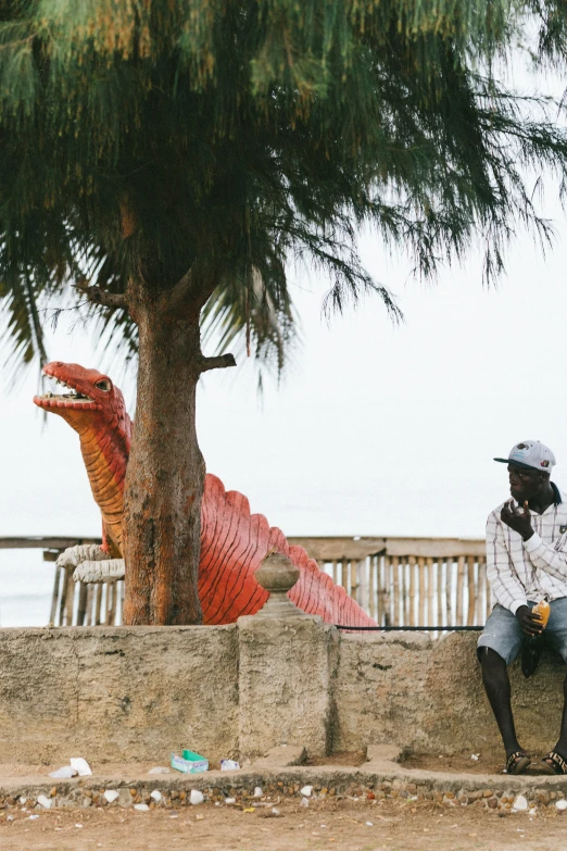 a person wearing a helmet is sitting under a tree near large red alligator sculptures