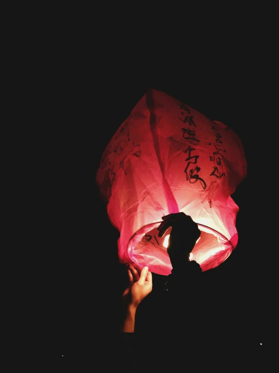 a person holding onto a chinese lantern in the dark