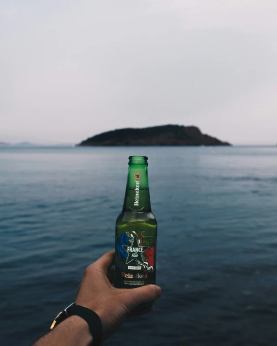 someone holding a beer bottle in front of the ocean