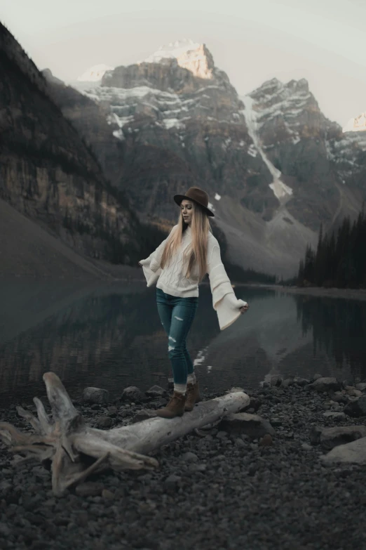 a woman stands near the edge of a body of water with snowy mountains in the distance