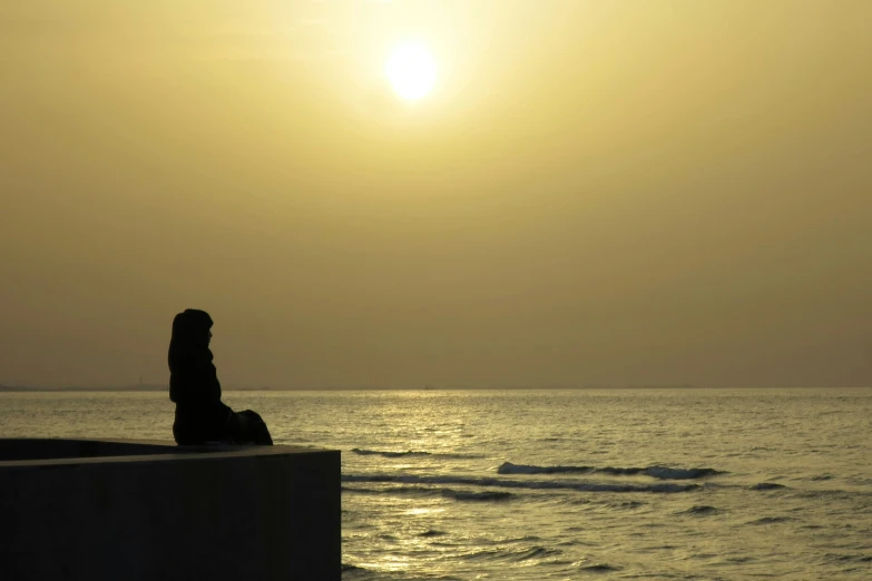 the silhouette of a person sitting on the edge of a pier