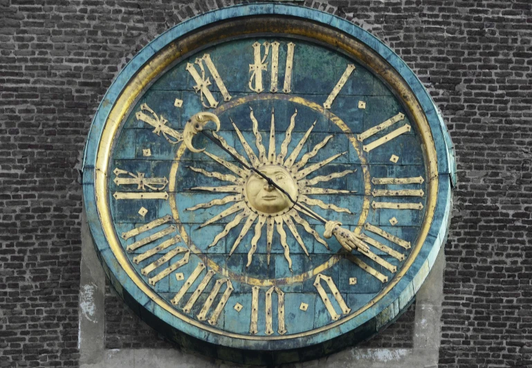 a blue and gold roman numeral clock on a brick wall