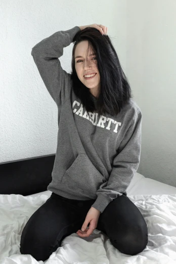a girl sitting on a bed wearing a sweatshirt