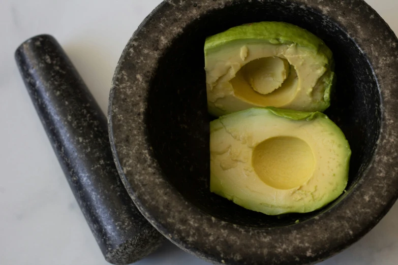 a mortar bowl filled with an avocado and two black tongs