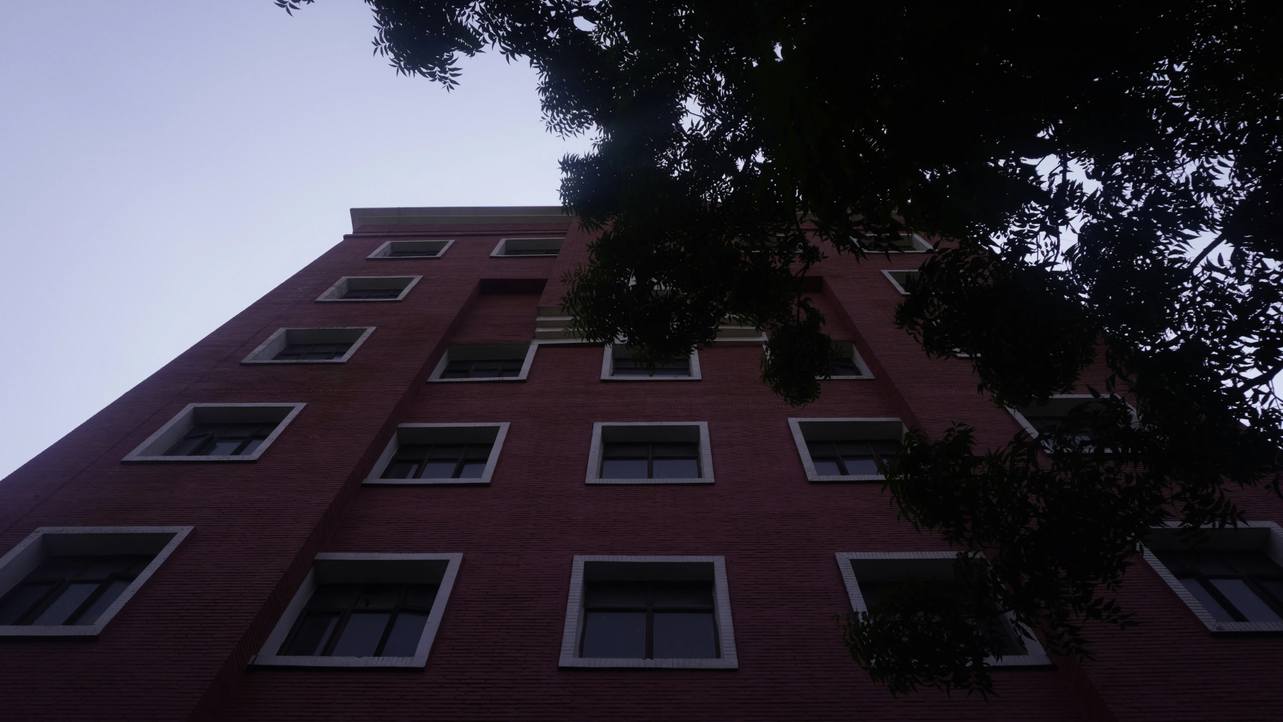 the windows of a red brick building are partially obscured by trees