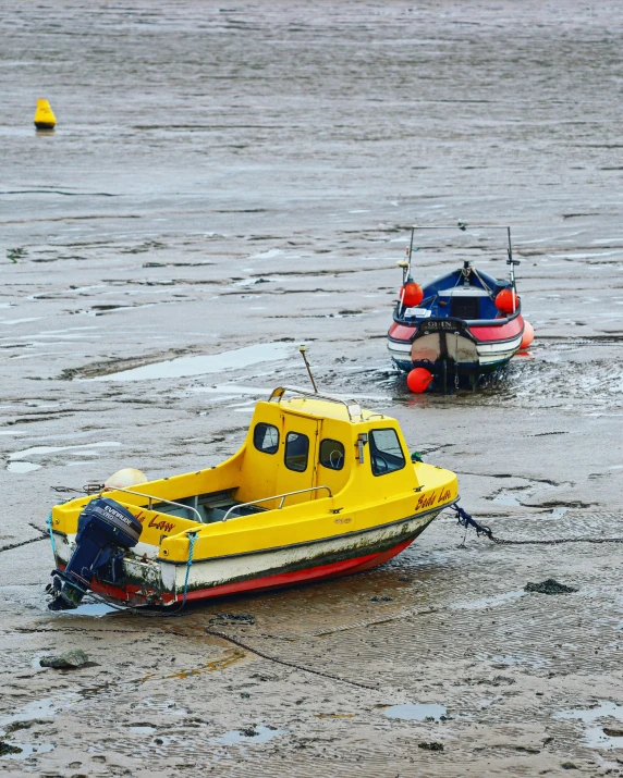 two small boats sit on mud on a beach