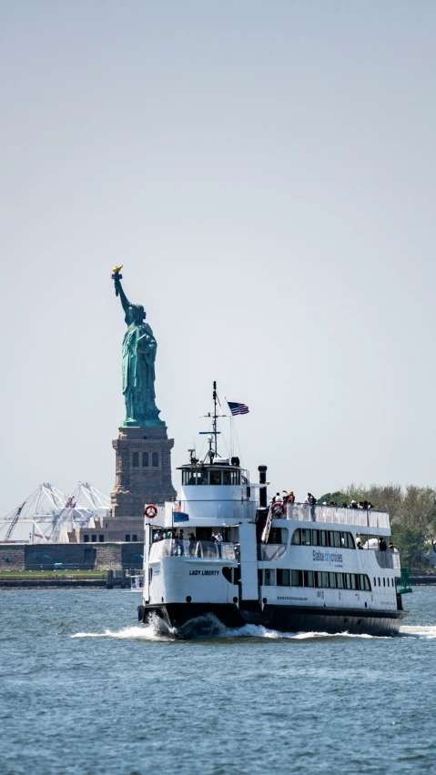 a ferry with statue of liberty on background during daytime