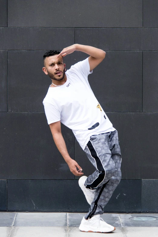 the young man is standing by the wall in his white shirt