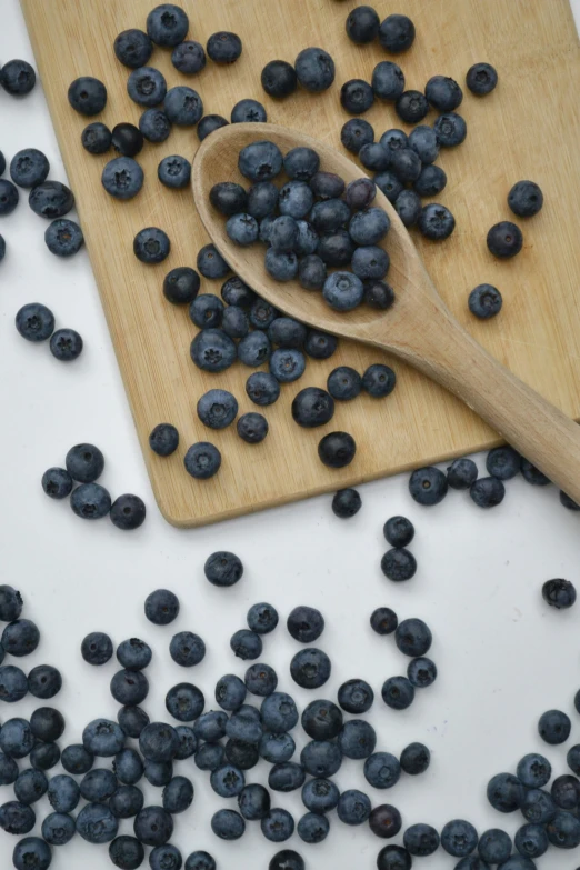 fresh blueberries scattered around a wooden spoon on a  board